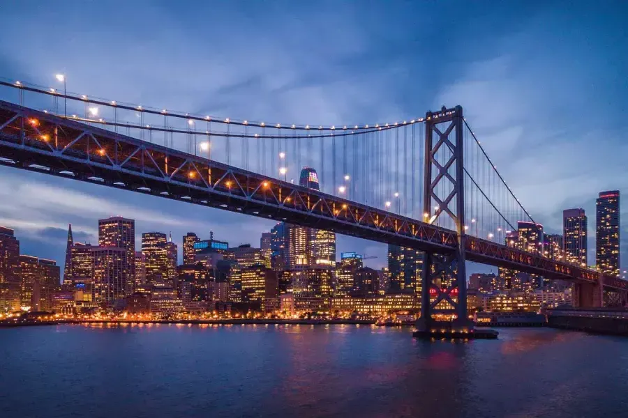 Die Bay Bridge und die Uferpromenade von Embarcardero sind nachts beleuchtet.