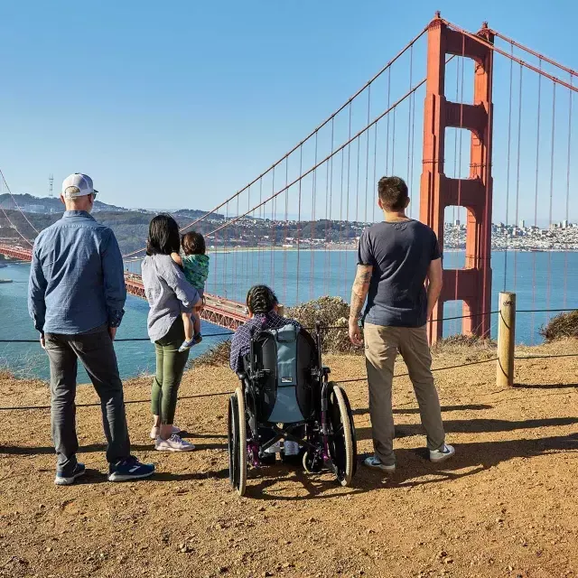 車椅子に乗った人を含む一団が、マリン・ヘッドランズからGolden Gate Bridgeを後ろから眺めている様子。